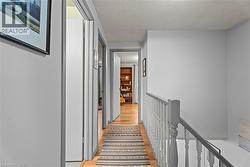 Hallway featuring an upstairs landing, a textured ceiling, and light wood finished floors - 