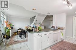 Kitchen with white cabinets, light tile patterned flooring, a peninsula, white dishwasher, and dark countertops - 