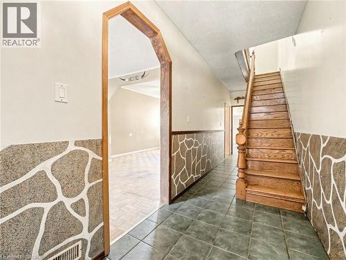 Stairs featuring tile patterned floors, a textured ceiling, wainscoting, and arched walkways - 23 Oak Avenue, Hamilton, ON - Indoor Photo Showing Other Room