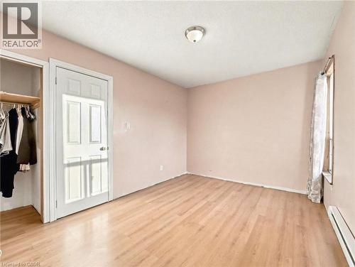 Unfurnished bedroom featuring a baseboard radiator, light wood-style floors, and a textured ceiling - 23 Oak Avenue, Hamilton, ON - Indoor Photo Showing Other Room