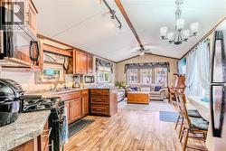 Kitchen featuring black appliances, brown cabinetry, lofted ceiling, light wood-style floors, and a chandelier - 