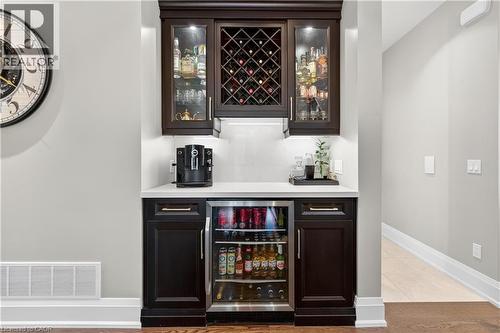 Indoor dry bar featuring wine cooler, dark brown cabinetry, glass insert cabinets, light stone countertops, and light tile patterned floors - 18 David Avenue, Hamilton, ON - Indoor Photo Showing Other Room