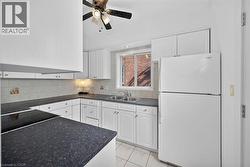 Kitchen with freestanding refrigerator, white cabinets, dark countertops, light tile patterned flooring, and backsplash - 