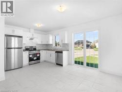 Kitchen featuring stainless steel appliances, decorative backsplash, white cabinetry, under cabinet range hood, and light countertops - 