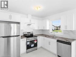 Kitchen with appliances with stainless steel finishes, white cabinets, under cabinet range hood, and backsplash - 