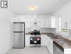 Kitchen featuring appliances with stainless steel finishes, light marble finish floors, tasteful backsplash, and white cabinets - 