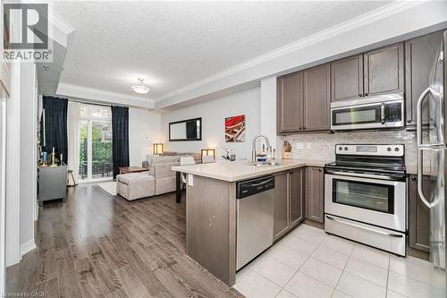 Kitchen featuring appliances with stainless steel finishes, dark brown cabinets, a peninsula, ornamental molding, and open floor plan - 5317 Upper Middle Road Unit# 112, Burlington, ON - Indoor Photo Showing Kitchen