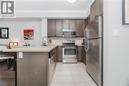 Kitchen with stainless steel appliances, a peninsula, crown molding, tasteful backsplash, and dark brown cabinets - 5317 Upper Middle Road Unit# 112, Burlington, ON - Indoor Photo Showing Kitchen