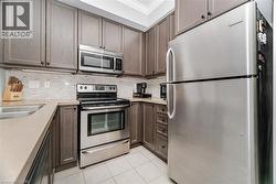 Kitchen featuring appliances with stainless steel finishes, crown molding, backsplash, light tile patterned flooring, and dark brown cabinets - 
