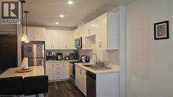 Kitchen with hanging light fixtures, white cabinets, dark wood finished floors, appliances with stainless steel finishes, and recessed lighting - 