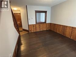 Empty room featuring dark wood-type flooring, a textured ceiling, wood walls, a wainscoted wall, and stairs - 