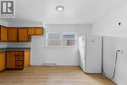 Kitchen featuring brown cabinetry, freestanding refrigerator, light wood finished floors, and dark countertops - 