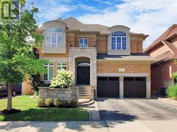 View of front of property featuring stone siding, a balcony, driveway, brick siding, and an attached garage - 