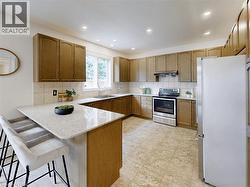 Kitchen with freestanding refrigerator, backsplash, stainless steel electric stove, a peninsula, and a kitchen bar - 