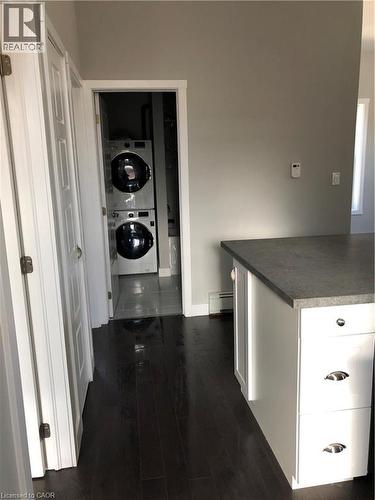 Hallway with stacked washing machine and dryer, dark wood-style flooring, and a baseboard radiator - 552 7Th Avenue, Hanover, ON - Indoor
