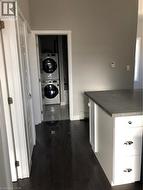 Hallway with stacked washing machine and dryer, dark wood-style flooring, and a baseboard radiator - 