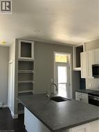 Kitchen with dark countertops, white cabinetry, an island with sink, dark wood-style floors, and stove - 