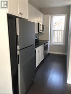 Kitchen featuring freestanding refrigerator, range, dark countertops, dark wood-style flooring, and white cabinetry - 
