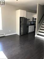 Kitchen with fridge, dark wood-style floors, stove, a baseboard radiator, and white cabinetry - 