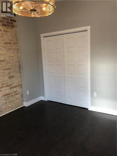 Unfurnished bedroom featuring dark wood-type flooring, a closet, a chandelier, and brick wall - 552 7Th Avenue, Hanover, ON - Indoor Photo Showing Other Room
