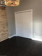 Unfurnished bedroom featuring dark wood-type flooring, a closet, a chandelier, and brick wall - 