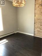 Unfurnished room featuring dark wood finished floors, baseboard heating, and a chandelier - 