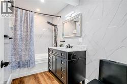 Bathroom with shower / bath combination with curtain, stone wall, tile walls, vanity, and light wood-style floors - 