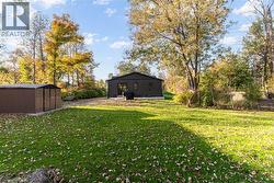 View of grassy yard featuring a storage unit, a patio, and view of scattered trees - 