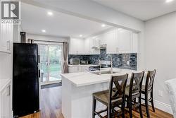 Kitchen with light wood finished floors, white cabinetry, freestanding refrigerator, backsplash, and recessed lighting - 