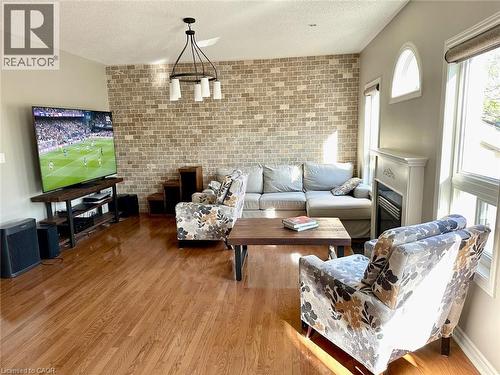 Living room featuring wood finished floors, a textured ceiling, brick wall, and a glass covered fireplace - 2429 Whitehorn Drive, Burlington, ON - Indoor Photo Showing Living Room