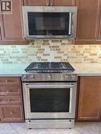 Kitchen featuring stainless steel appliances, light countertops, light tile patterned flooring, and tasteful backsplash - 