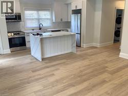 Kitchen with a center island, stainless steel appliances, white cabinets, light stone counters, and light wood finished floors - 