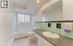 Full bath featuring shower / bathtub combination, vanity, a baseboard heating unit, light wood finished floors, and tile walls - 