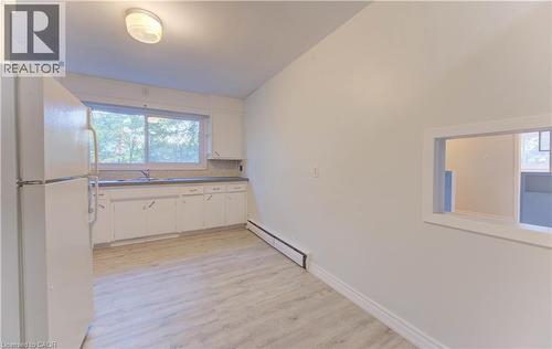 Kitchen with freestanding refrigerator, white cabinets, baseboard heating, and plenty of natural light - 50 Gordon Avenue, Kitchener, ON - Indoor