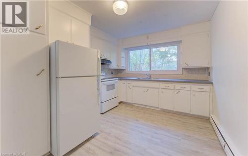 Kitchen featuring white appliances, a baseboard radiator, white cabinets, light wood-style flooring, and backsplash - 50 Gordon Avenue, Kitchener, ON - Indoor Photo Showing Kitchen With Double Sink