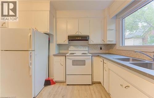 Kitchen with white appliances, light wood-style floors, under cabinet range hood, and white cabinets - 50 Gordon Avenue, Kitchener, ON - Indoor Photo Showing Kitchen With Double Sink