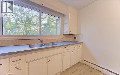Kitchen featuring a baseboard heating unit, white cabinetry, decorative backsplash, and light wood-style floors - 50 Gordon Avenue, Kitchener, ON - Indoor Photo Showing Kitchen With Double Sink