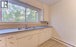 Kitchen featuring a baseboard heating unit, white cabinetry, decorative backsplash, and light wood-style floors - 