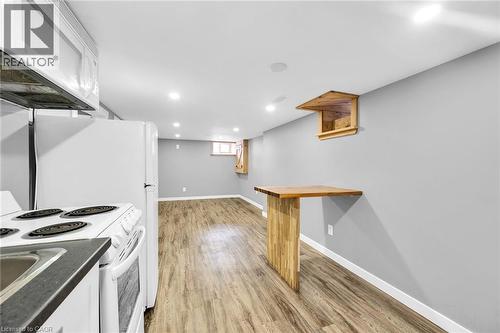 Kitchen featuring white appliances, white cabinets, light wood finished floors, baseboards, and dark countertops - 129 Dundurn Street N, Hamilton, ON - Indoor