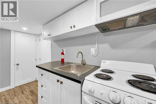 Kitchen with white electric range oven, a sink, dark countertops, white cabinets, and light wood-type flooring - 129 Dundurn Street N, Hamilton, ON - Indoor Photo Showing Kitchen