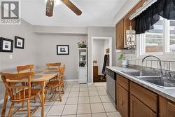 Kitchen with brown cabinets, stainless steel dishwasher, light countertops, light tile patterned floors, and ceiling fan - 
