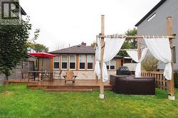 Back of property featuring a wooden deck, a hot tub, a chimney, stone siding, and roof with shingles - 