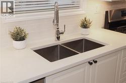 Kitchen view of white cabinetry, stainless steel stove, decorative backsplash, and light stone countertops - 