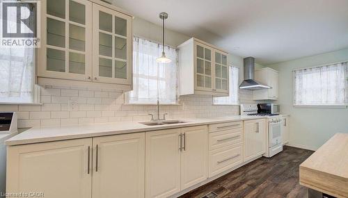 Kitchen featuring white range with gas stovetop, wall chimney range hood, glass insert cabinets, tasteful backsplash, and dark wood finished floors - 14 Grandview Street, Brantford, ON - Indoor Photo Showing Kitchen With Double Sink