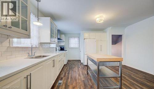 Kitchen with glass insert cabinets, backsplash, white appliances, wall chimney range hood, and dark wood-style floors - 14 Grandview Street, Brantford, ON - Indoor Photo Showing Kitchen With Double Sink