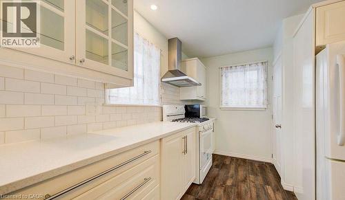 Kitchen with white appliances, wall chimney range hood, dark wood-style floors, glass insert cabinets, and tasteful backsplash - 14 Grandview Street, Brantford, ON - Indoor Photo Showing Kitchen