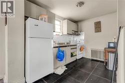 Kitchen featuring white appliances, radiator heating unit, white cabinets, tasteful backsplash, and exhaust hood - 