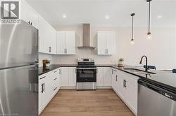 Kitchen featuring stainless steel appliances, wall chimney range hood, white cabinets, decorative light fixtures, and dark stone countertops - 