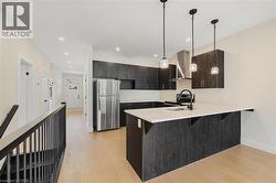 Kitchen featuring appliances with stainless steel finishes, a breakfast bar, wall chimney range hood, light wood-style floors, and a peninsula - 