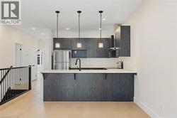 Kitchen with a peninsula, a breakfast bar area, freestanding refrigerator, decorative light fixtures, and light wood-style floors - 